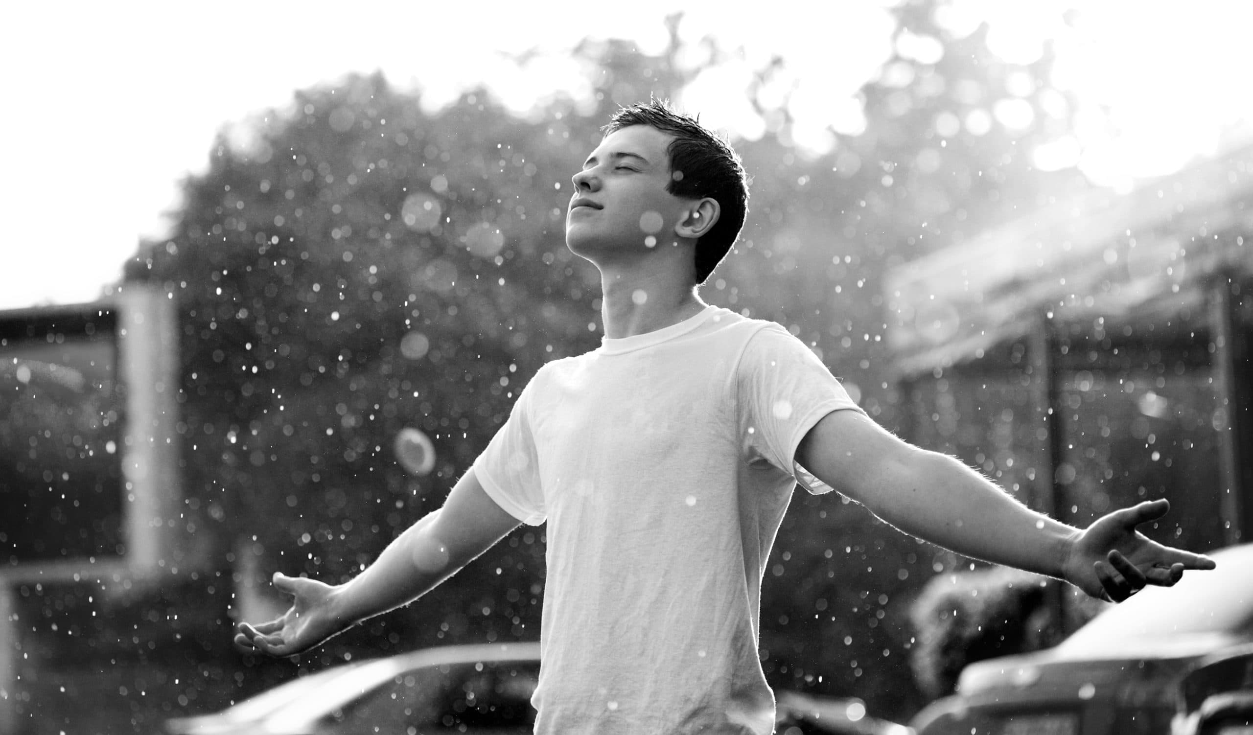 Boy standing with arms spread in the rain.